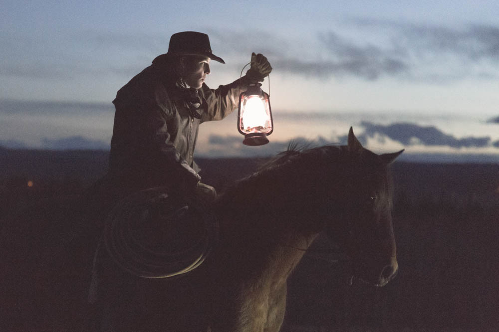 Image of a cowboy on a horse holding lantern in low light