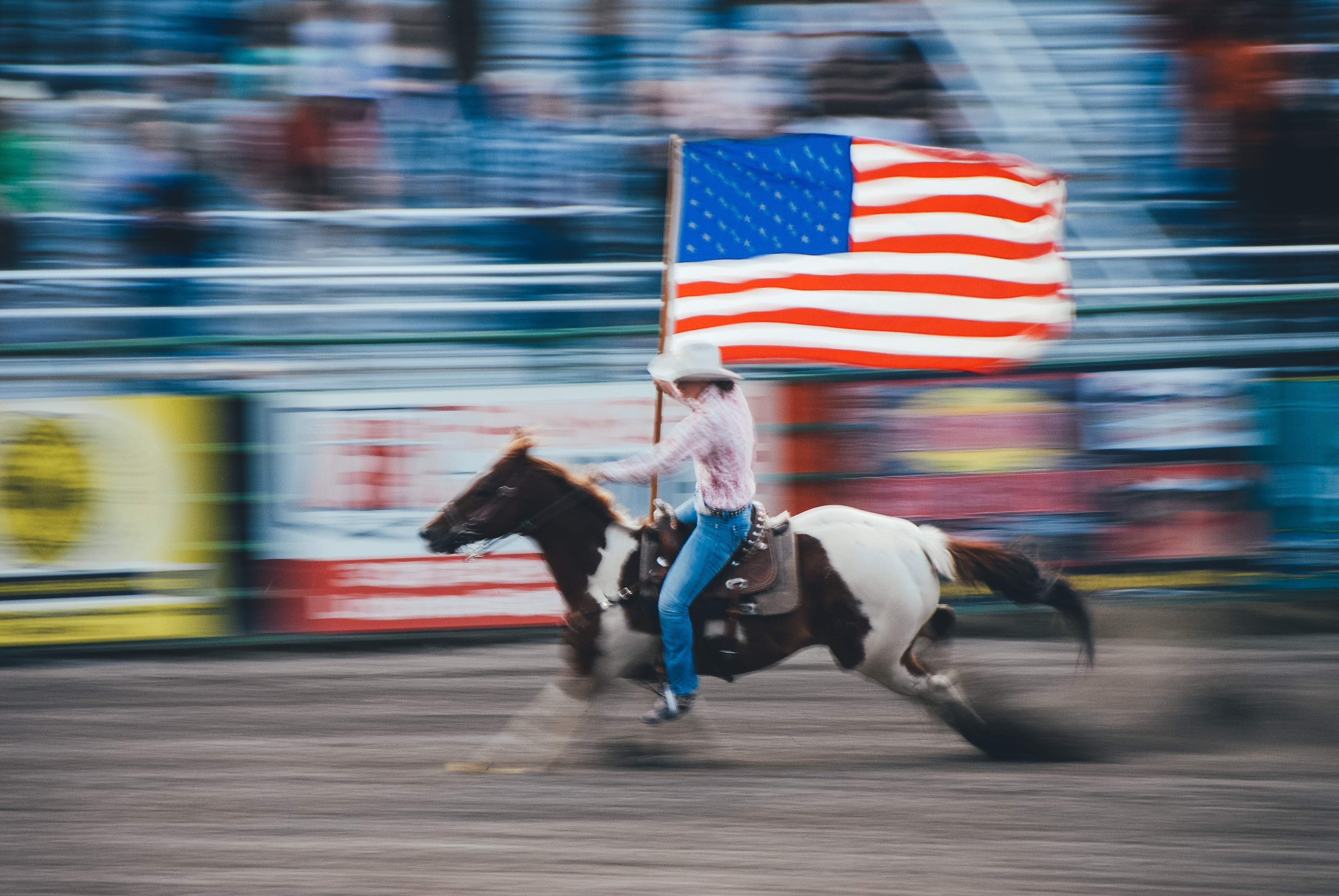 Image utilizing slow shutter speed and panning of a cowboy on a horse with an american flag
