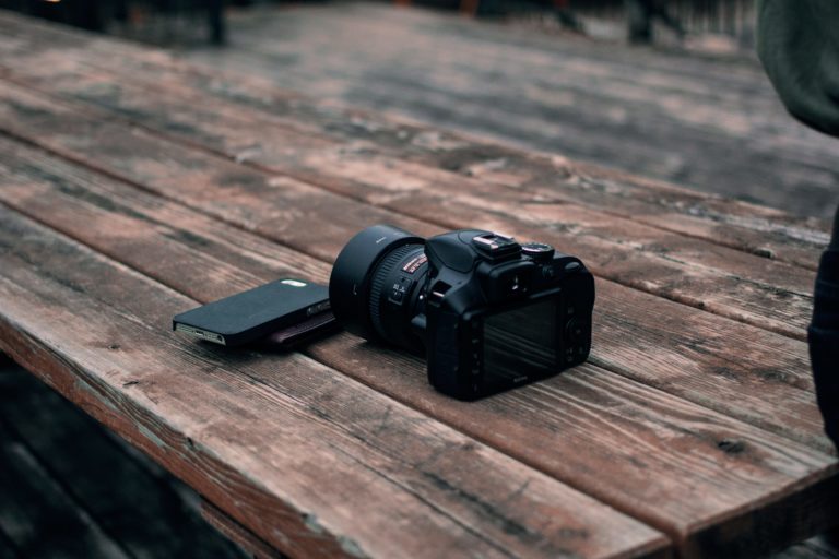 A DSLR and cellphone on a wood table.