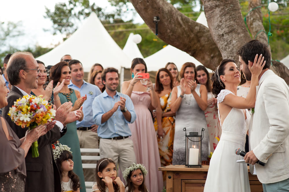 A bride putting her hand on the groom's cheek while wedding attendees applaud.