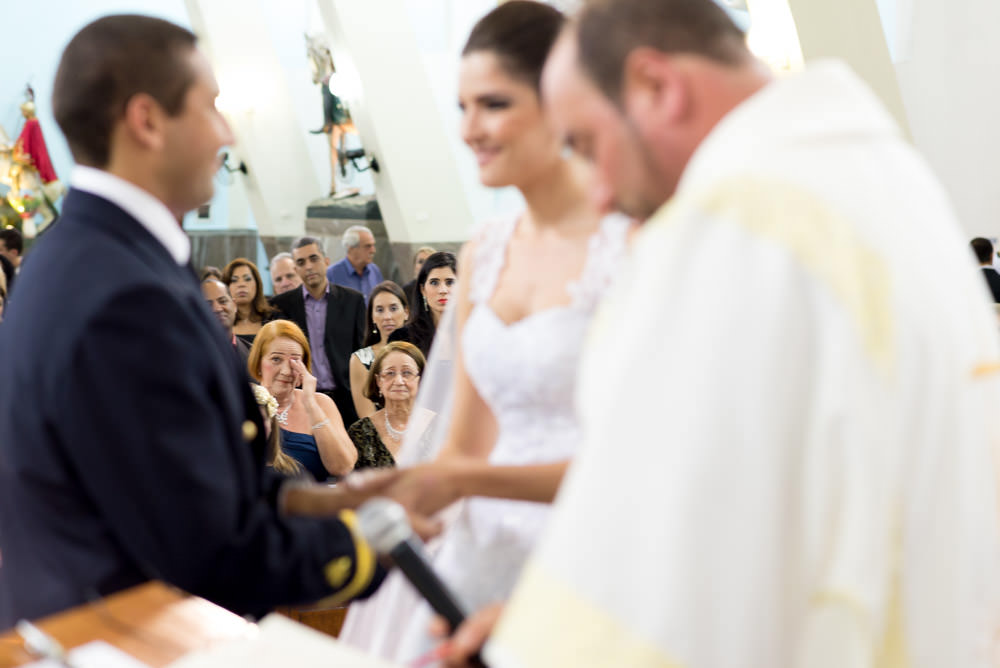 Picture taken during a wedding ceremony of a bride and groom giving their vows while a woman in the audience wipes a tear