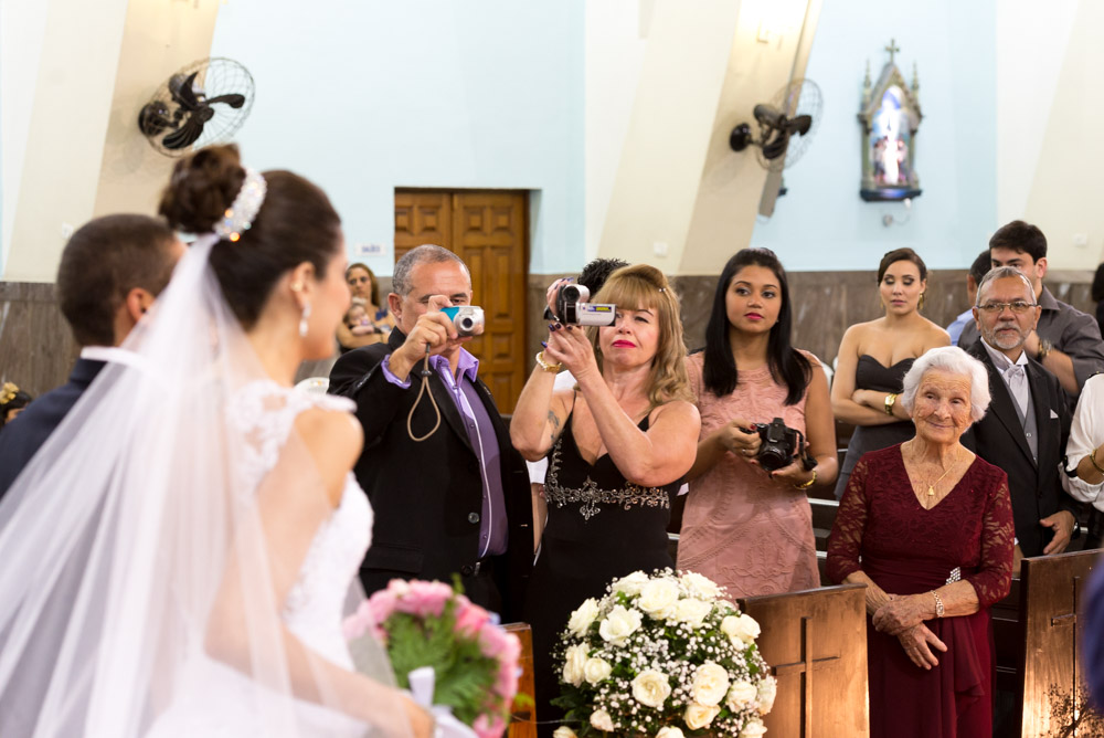 Image of a bride and groom shoot from an angle about to walk out the church after ceremony with grandma looking on and smiling