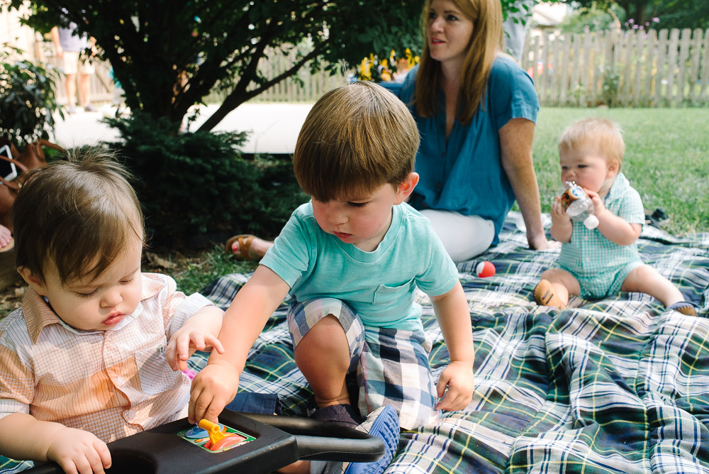 image of a one year old at his first birthday party playing with a toy and another boy