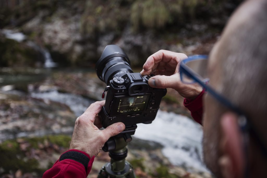 image of a photographer with glasses adjusting the aperture on his camera to make it wider for a blurred background effect