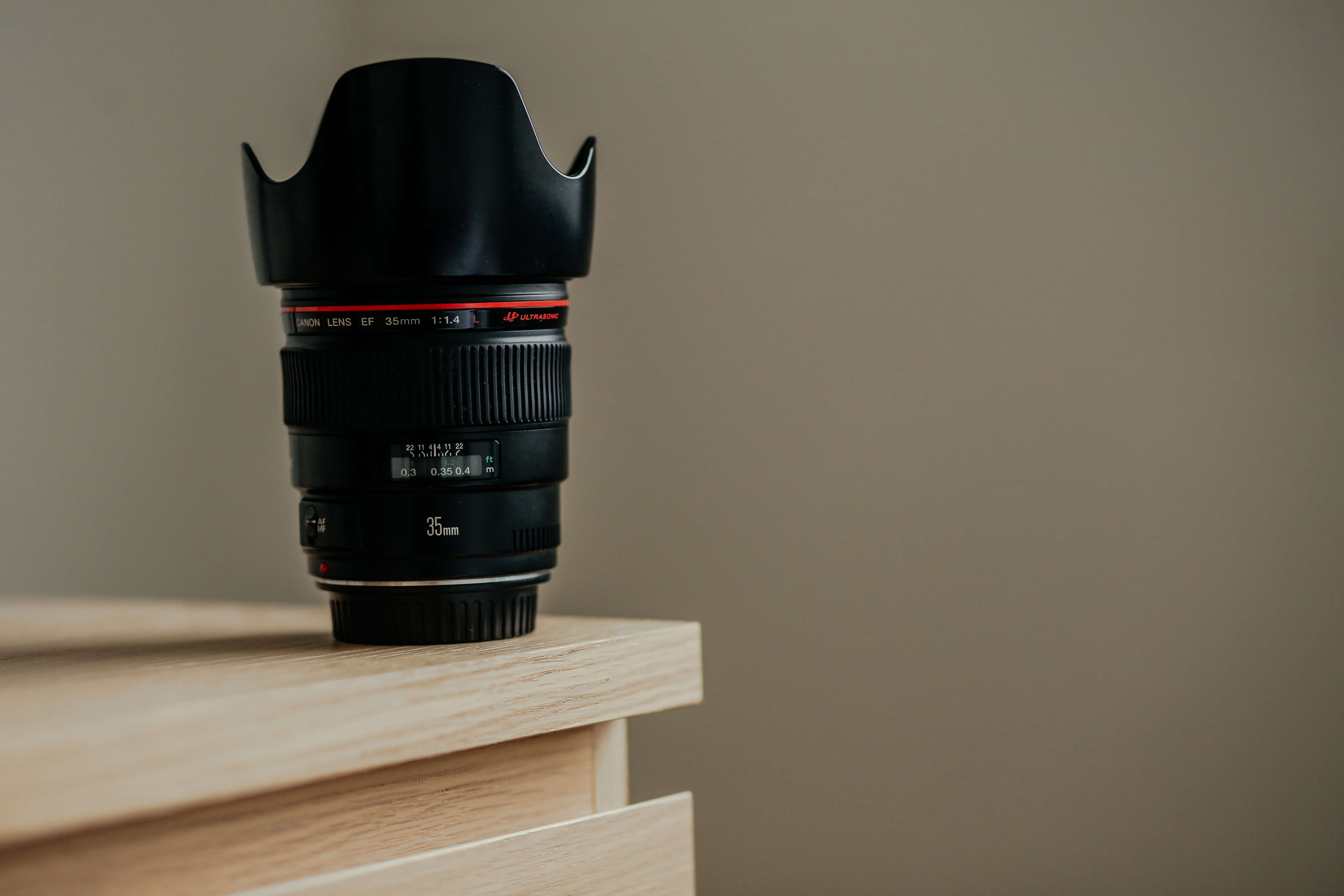 A Canon lens with a petal lens hood on a light-colored wood table.