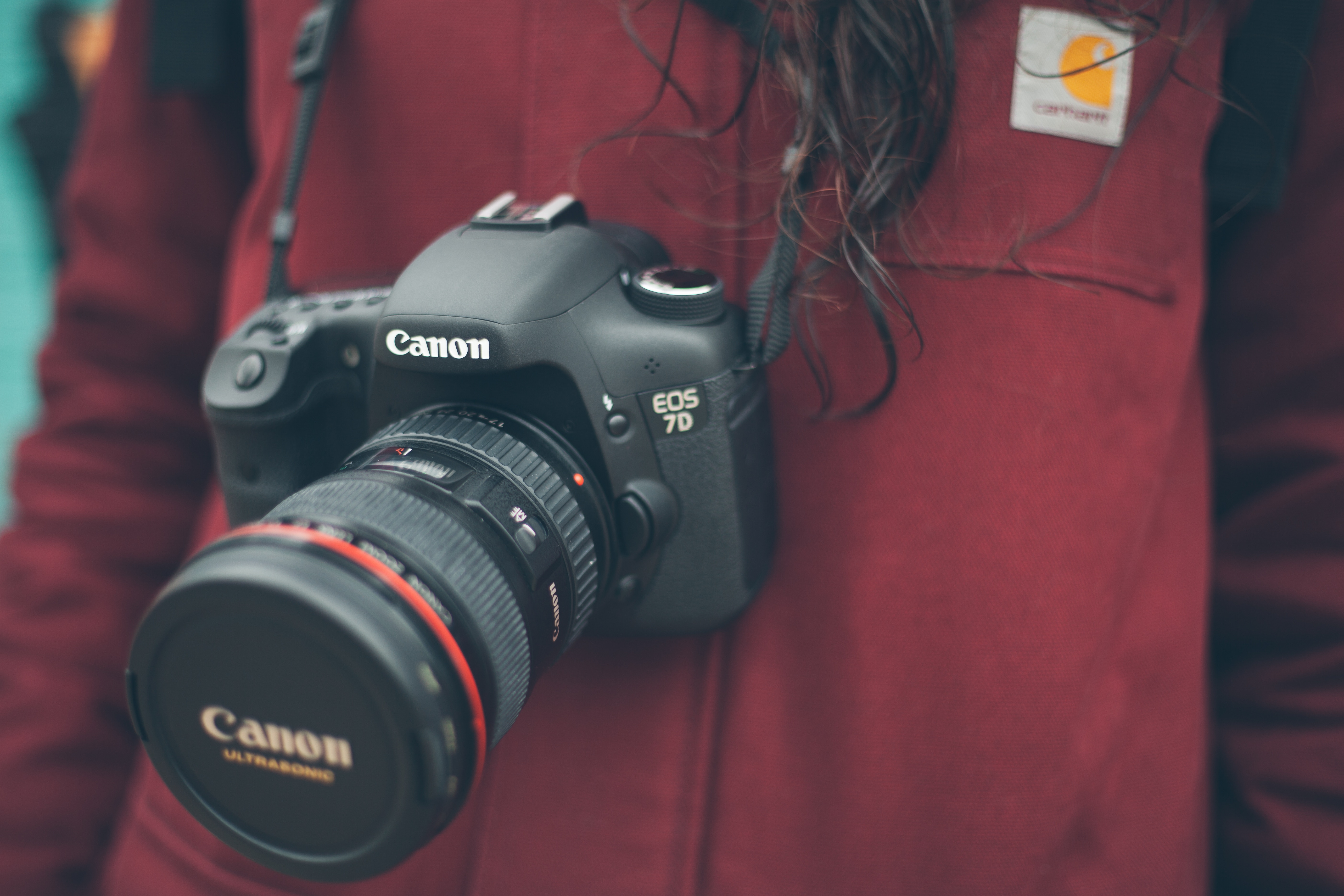 A DSLR hanging from a neck strep on a woman wearing a red coat.