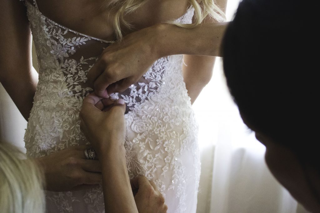 Photo of a bride getting help fastening her dress before her wedding