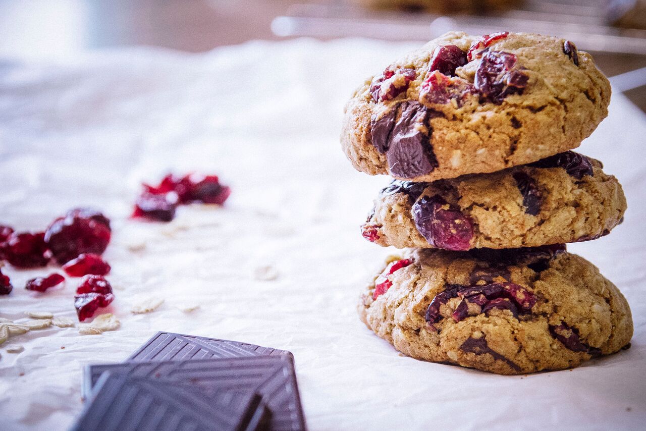 Three oatmeal chocolate chip cranberry cookies stacked on a white table.