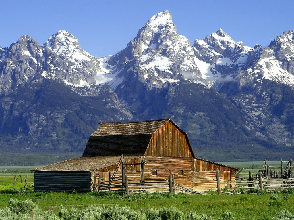 Image showing how to sell landscape photography work with a landscape of a barn in green grass in front of a mountain range and a blue sky