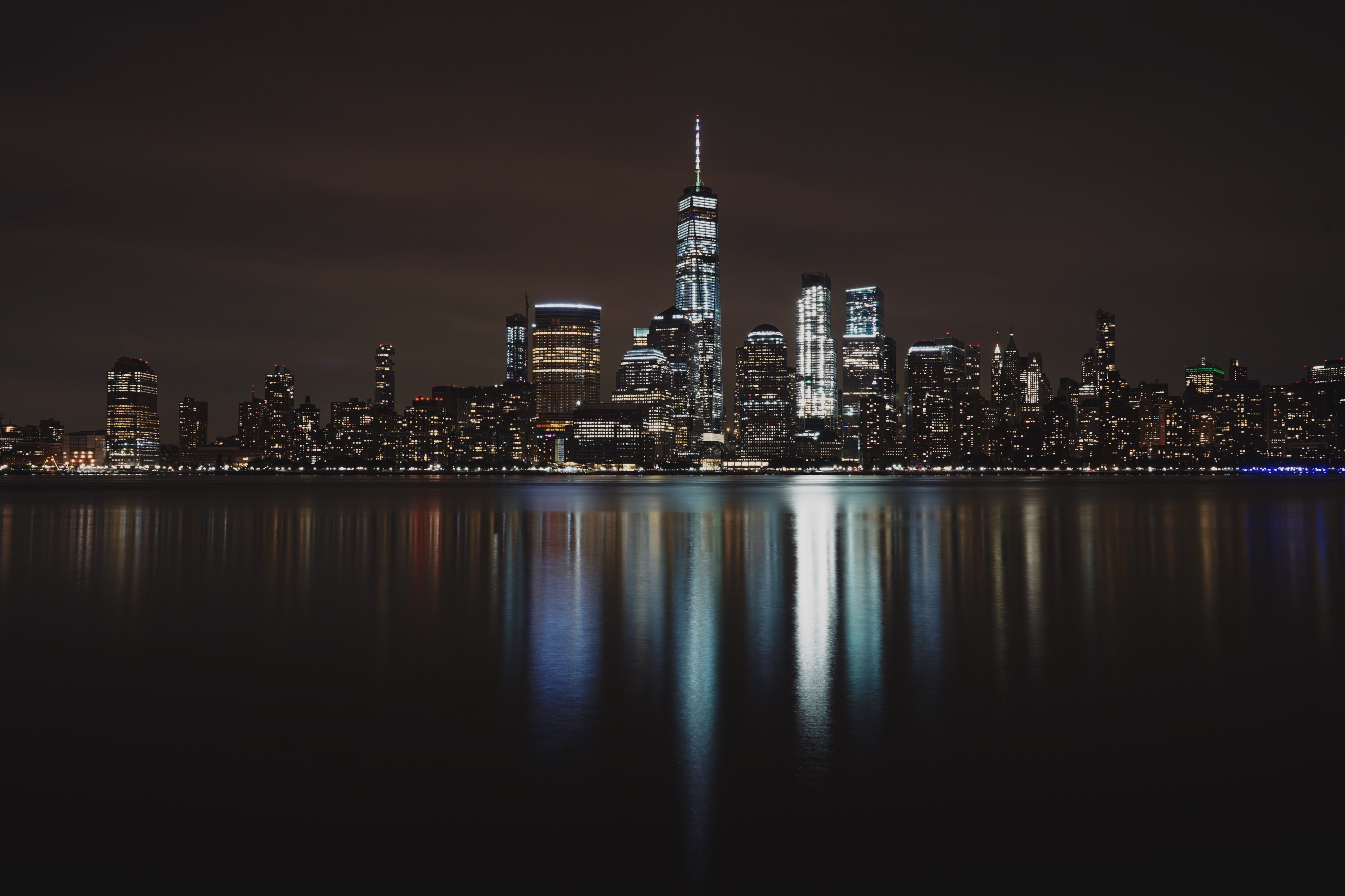 The New York City skyline and the lights from the building being reflected in water.