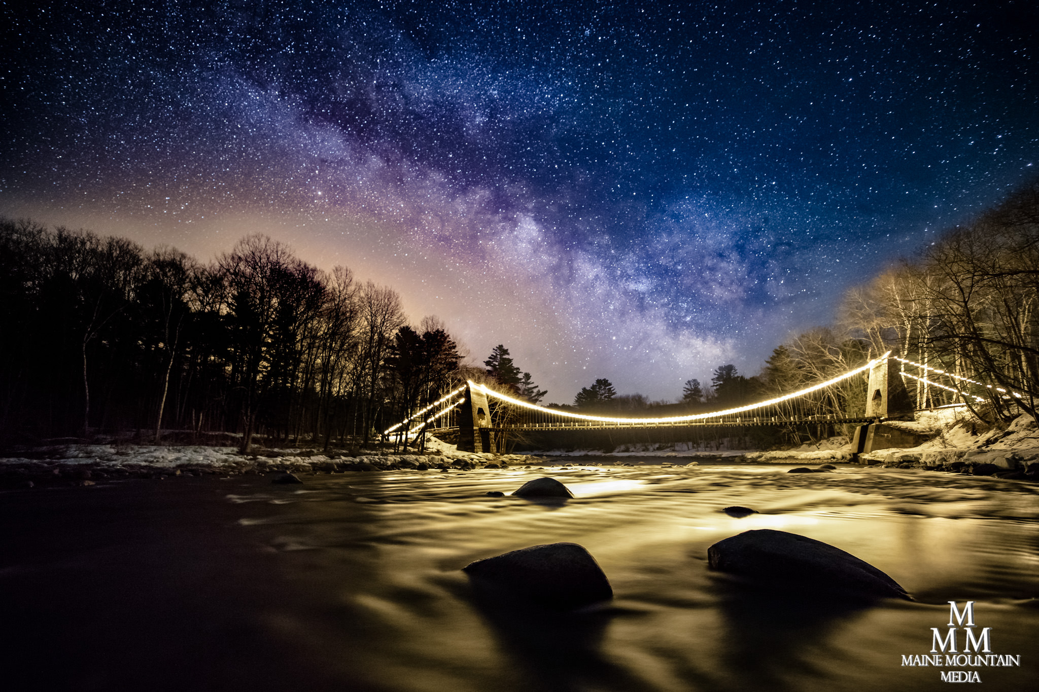 Image of a river with a lit up bridge and the Milky Way in the background