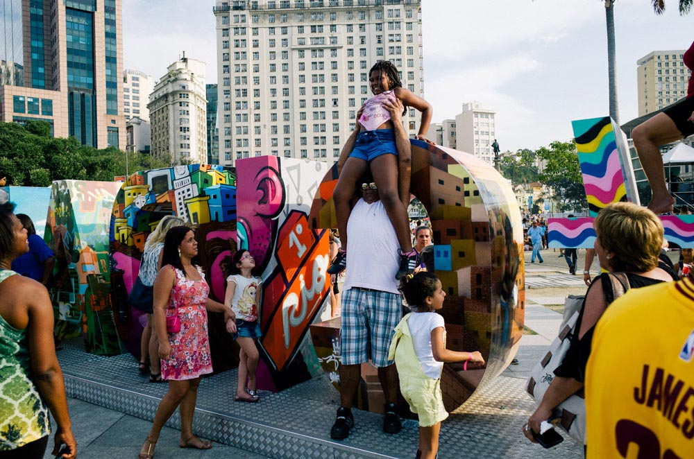 A man holding a girl up on a city decoration for the Rio de Janeiro Olympics.