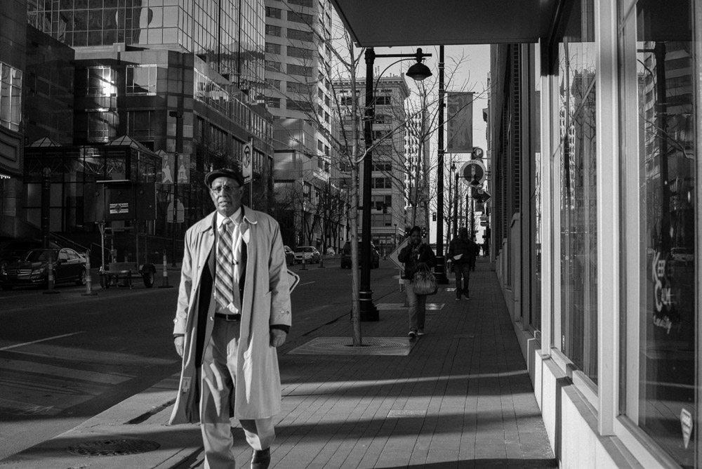 A man wearing a long trenchcoat walking down a sidewalk.