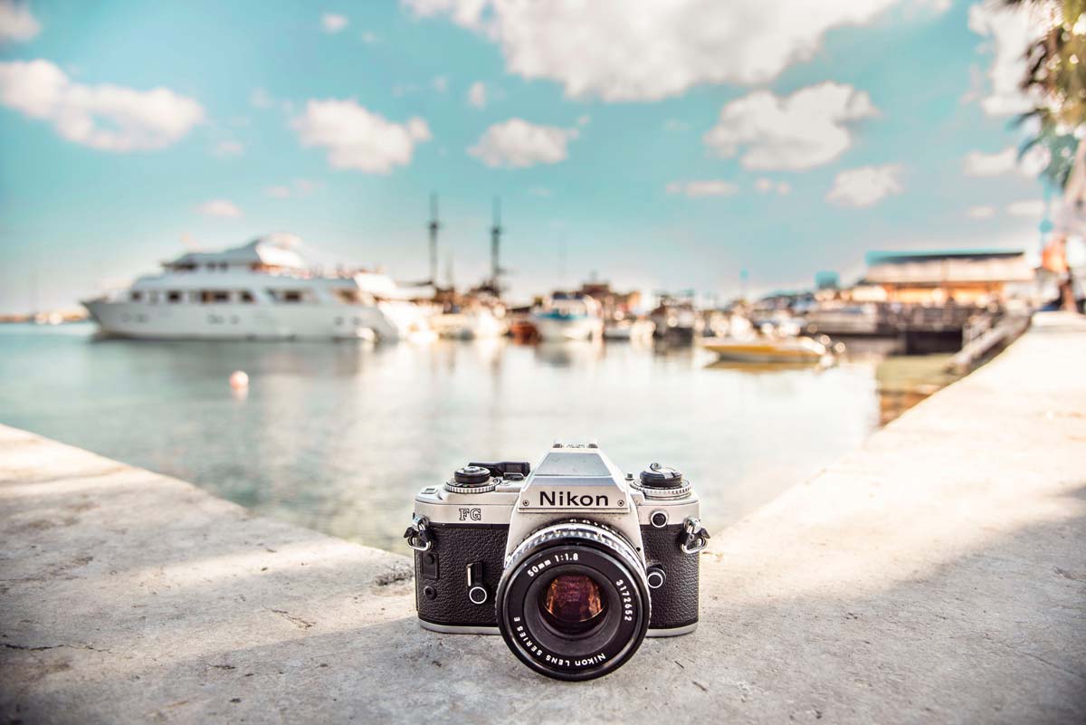 Image of a camera on a ledge in front of a bay with boats and a blue sky with some white clouds