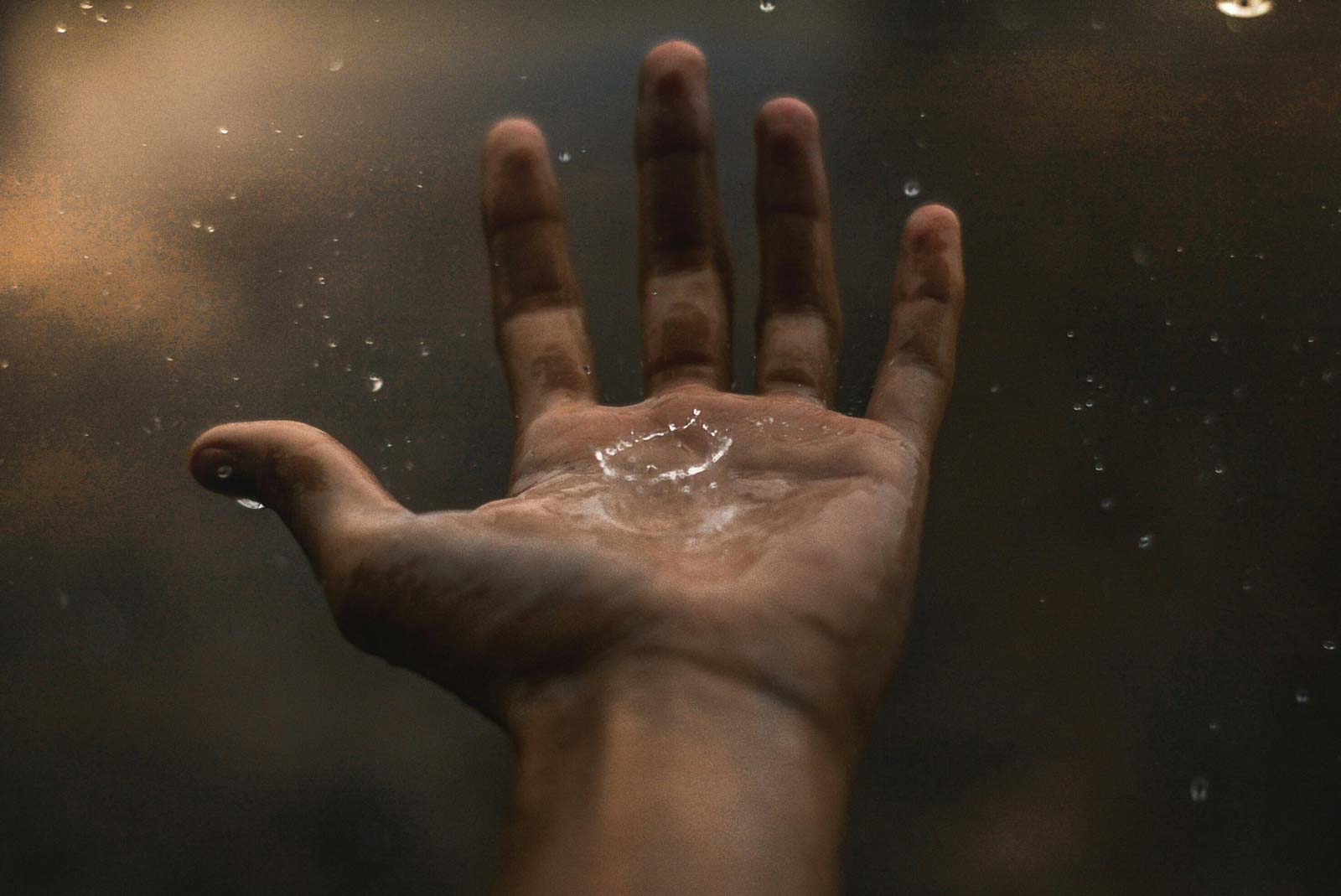 A person holding their hand out in rain.