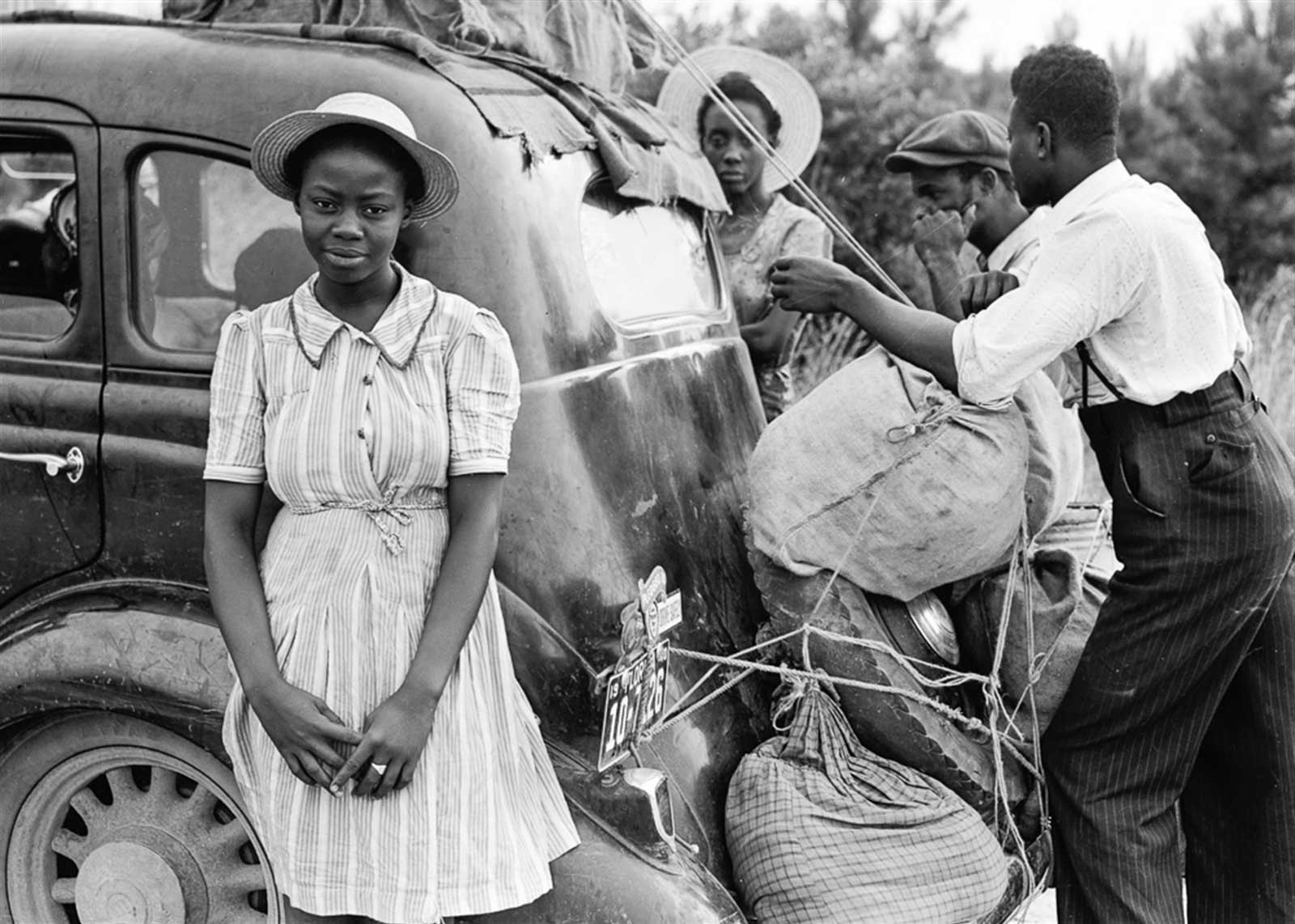 Vintage black and white photography of people loading stuff into a car with a woman looking into the camera