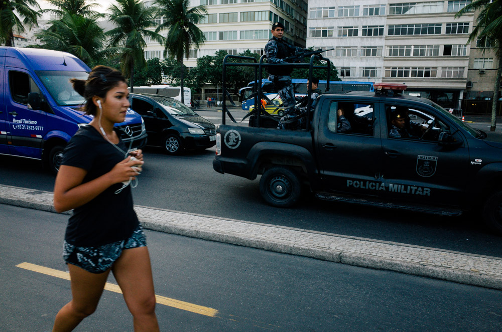 Street photography image of a woman running for exercise in Rio de Janeiro, Brazil, with a military vehicle behind her