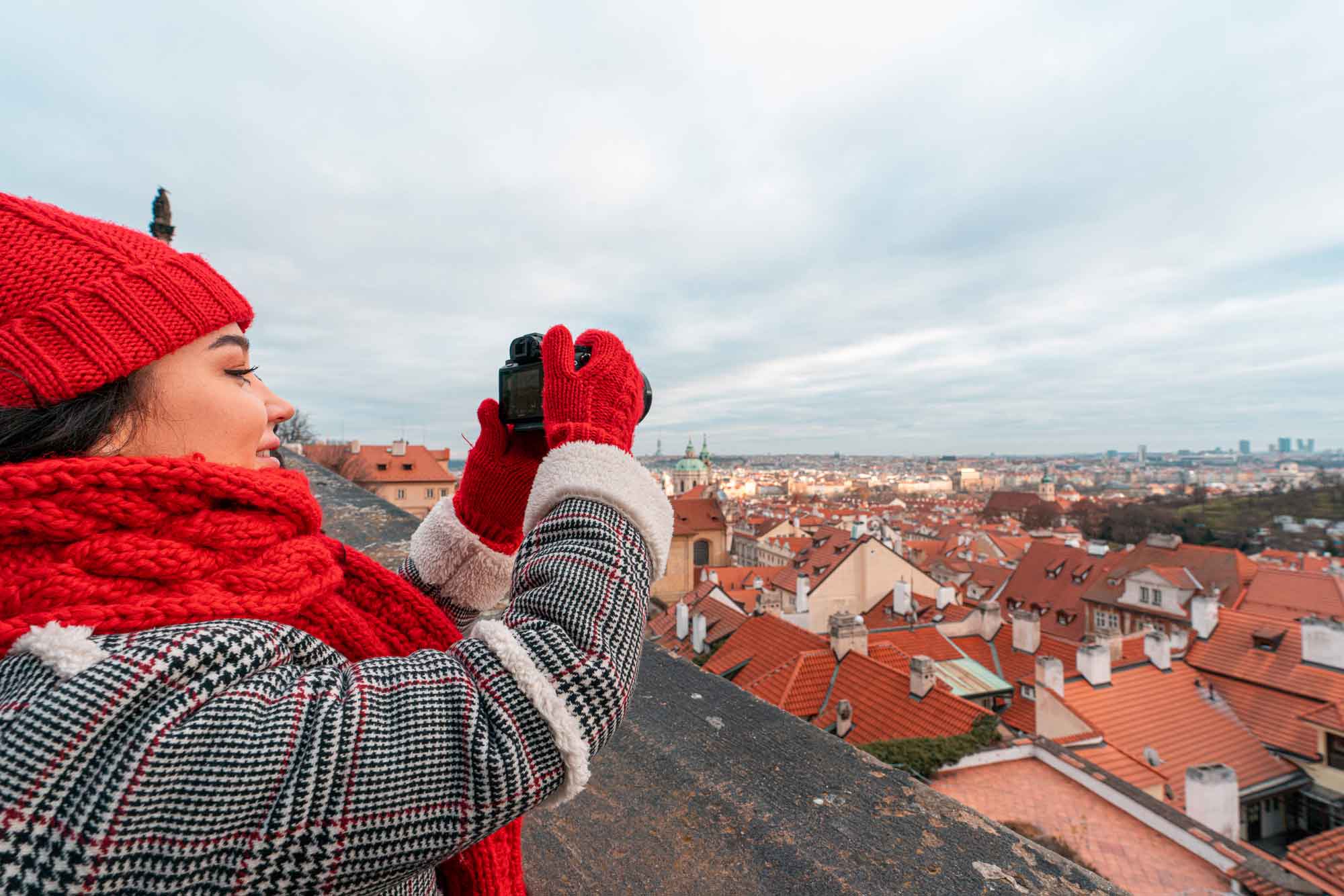 A woman in a red scarf and hat taking photos with a camera on a roof.