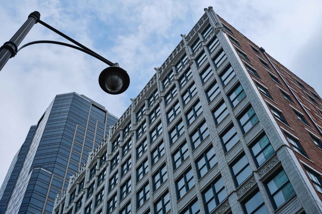 An old building and street lamp in front of a newer glass skyscraper.