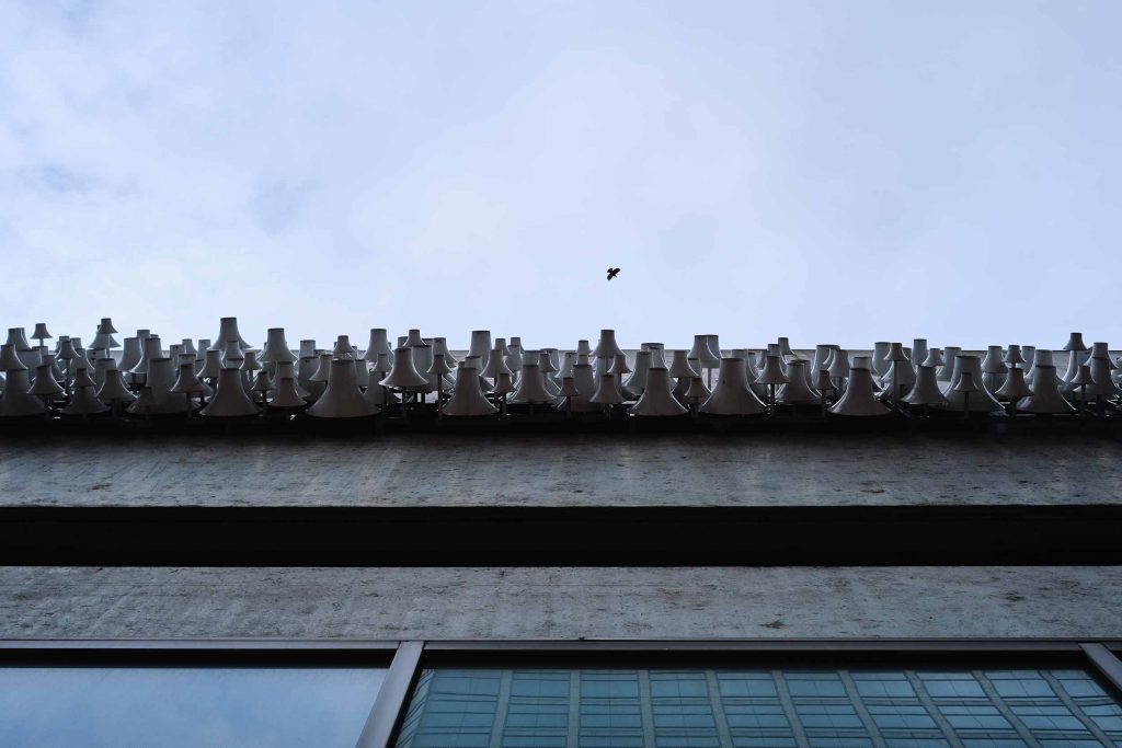 Looking up at a building with white metal cones on the side and a bird flying above.