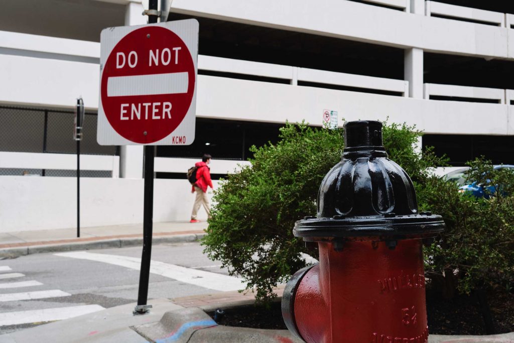 A red fire hydrant, a red and white do not enter sign, and a man wearing a red coat and red shoes across the street.