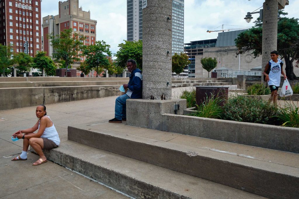 A woman and man sitting on a concrete platform as a teenage boy walks past.