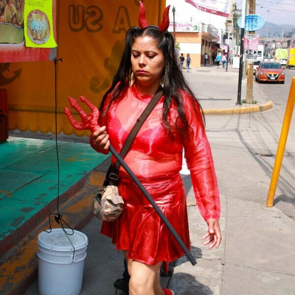 Brunette Mexican woman walking down a sidewalk wearing a red devil costume
