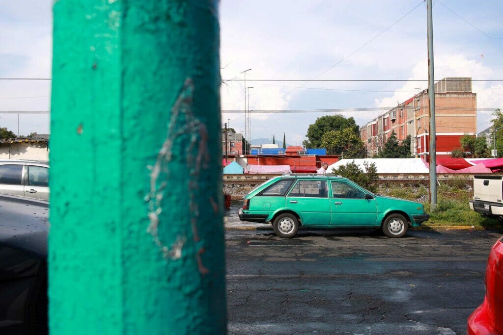 An old green car behind a green pole