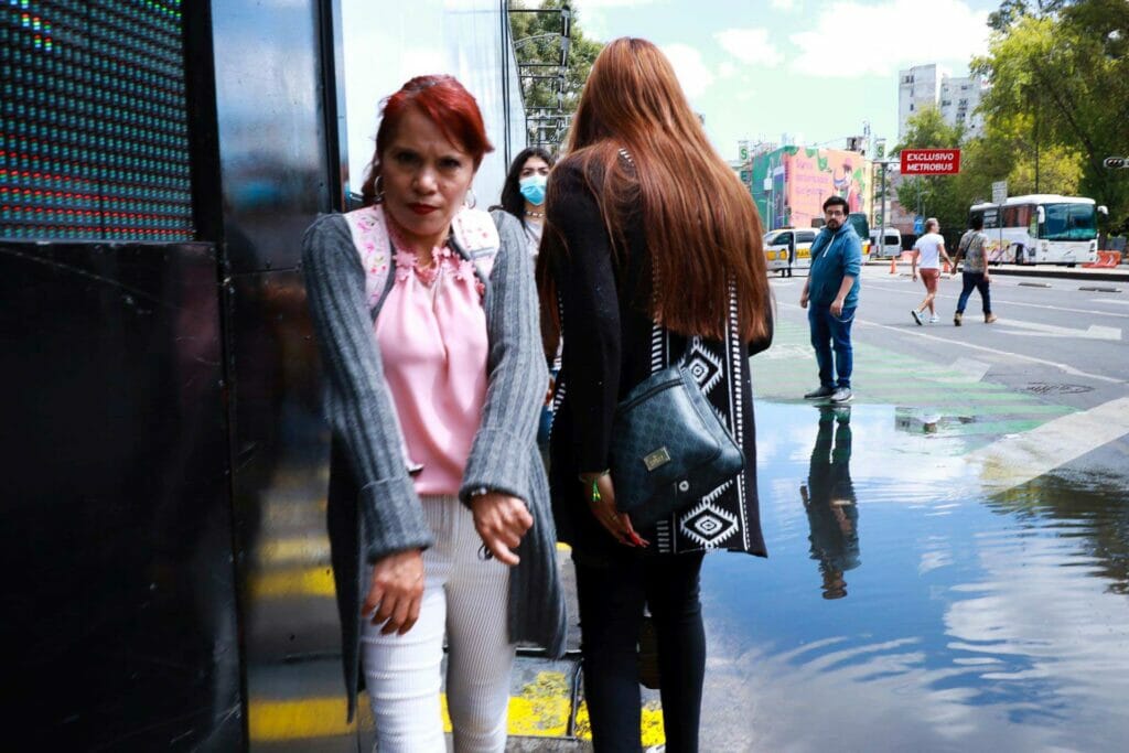 A woman walking down a sidewalk trying to avoid a large puddle.