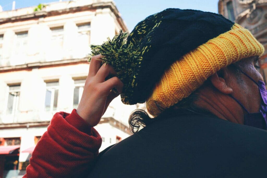 A child's arm grabbing an older man's knit hat.