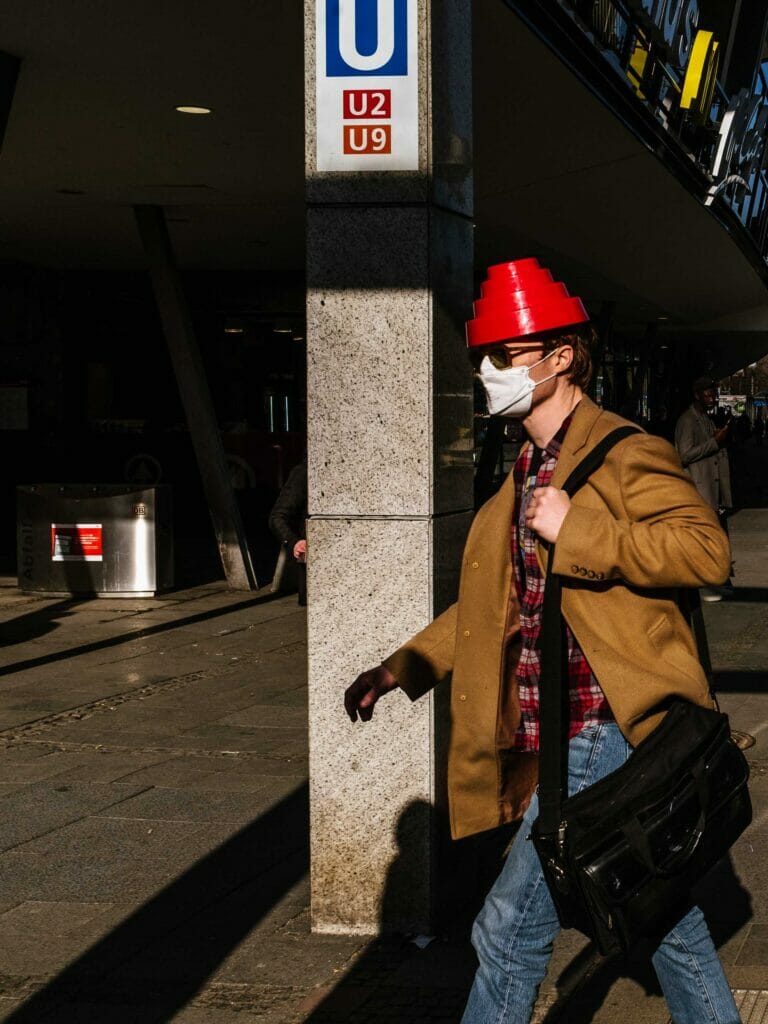 A man wearing a mask and red cone hat walking down a sidewalk.
