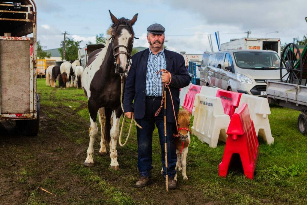 Man in hat holding the reins of a large horse and a small pony on either side