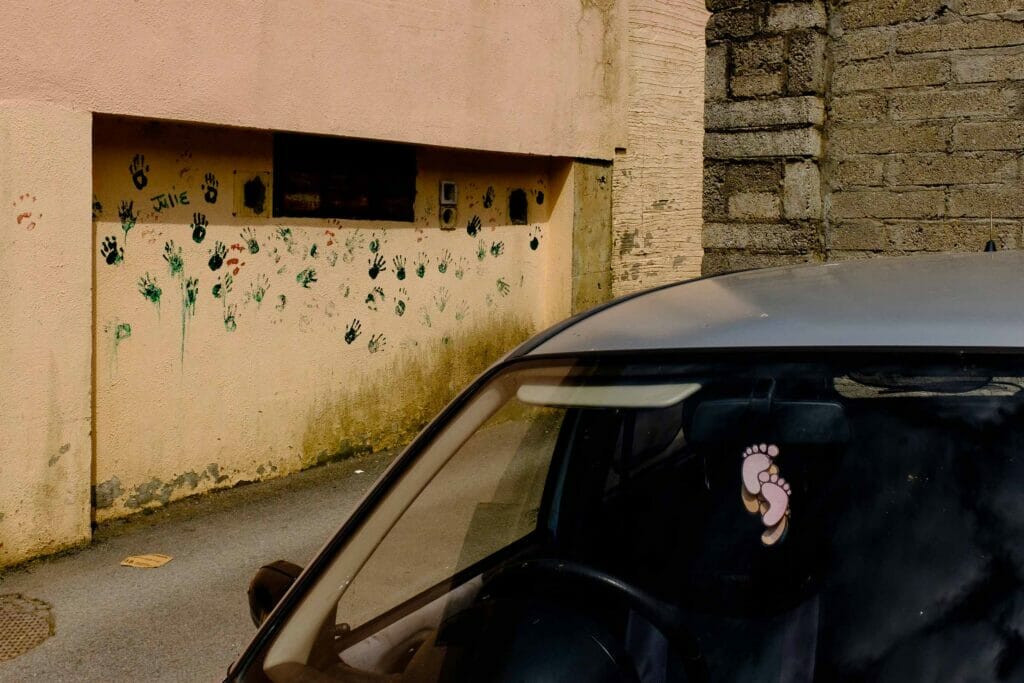 A car windshield where you can see dangling feet air fresheners by a wall with painted handprints.