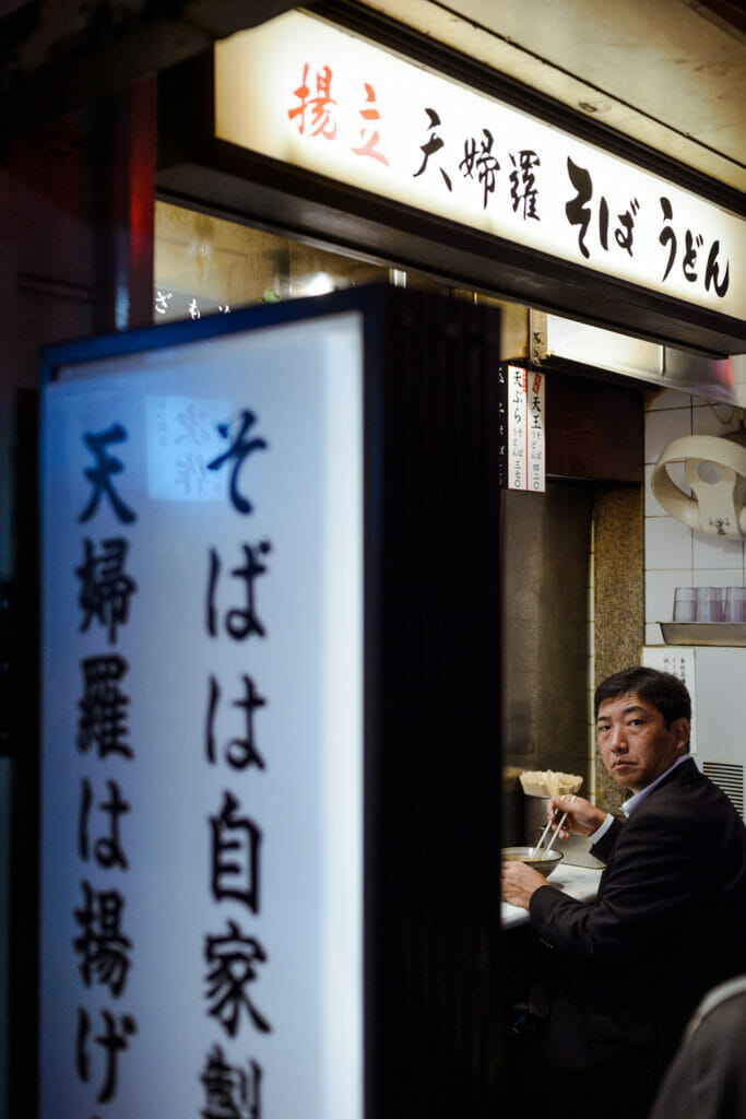 A man looking up from a noodle bowl in a restaurant.