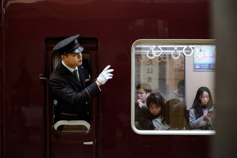 A train conductor looking out of window and passengers.