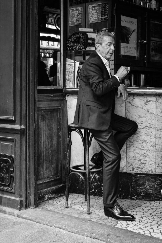 A man in a nice suit drinking espresso in a cafe.
