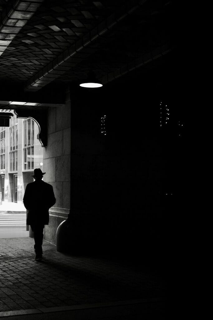 A man wearing a hat walking from shadow to light.