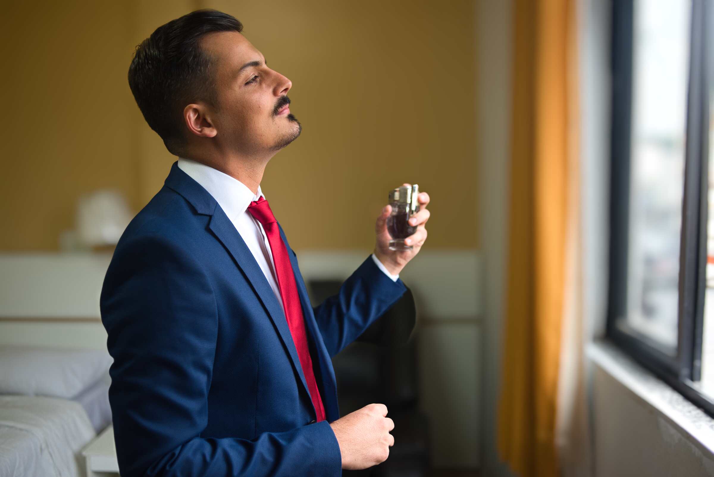 Portrait of a man by a window putting on cologne with bokeh applied to the background.