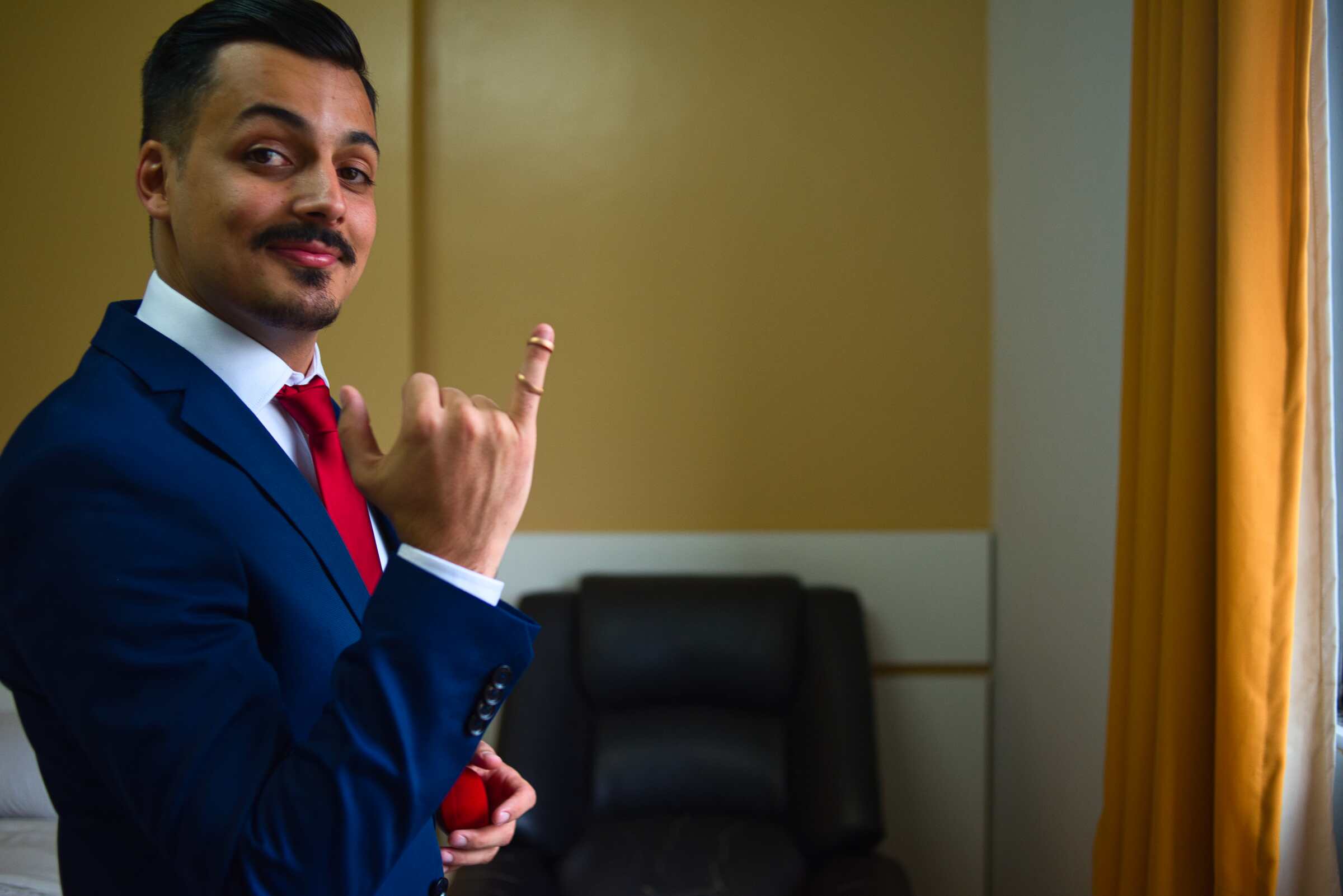 Portrait of a groom wearing a blue suit holding up wedding rings.