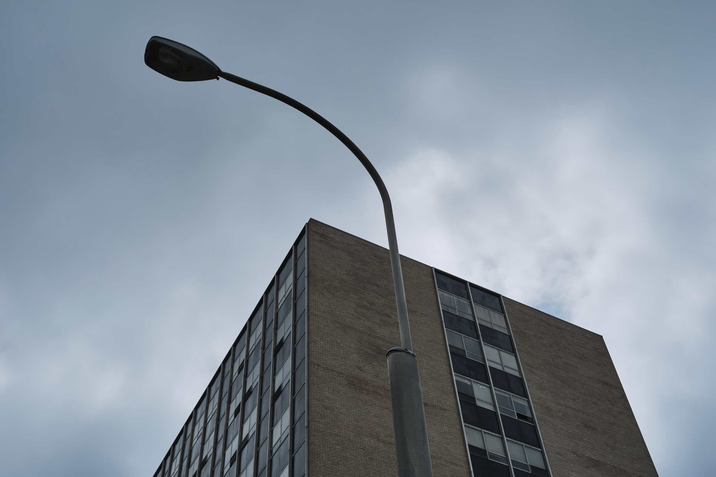 Looking up at a lamppost and a building and a gray cloudy sky with no editing.