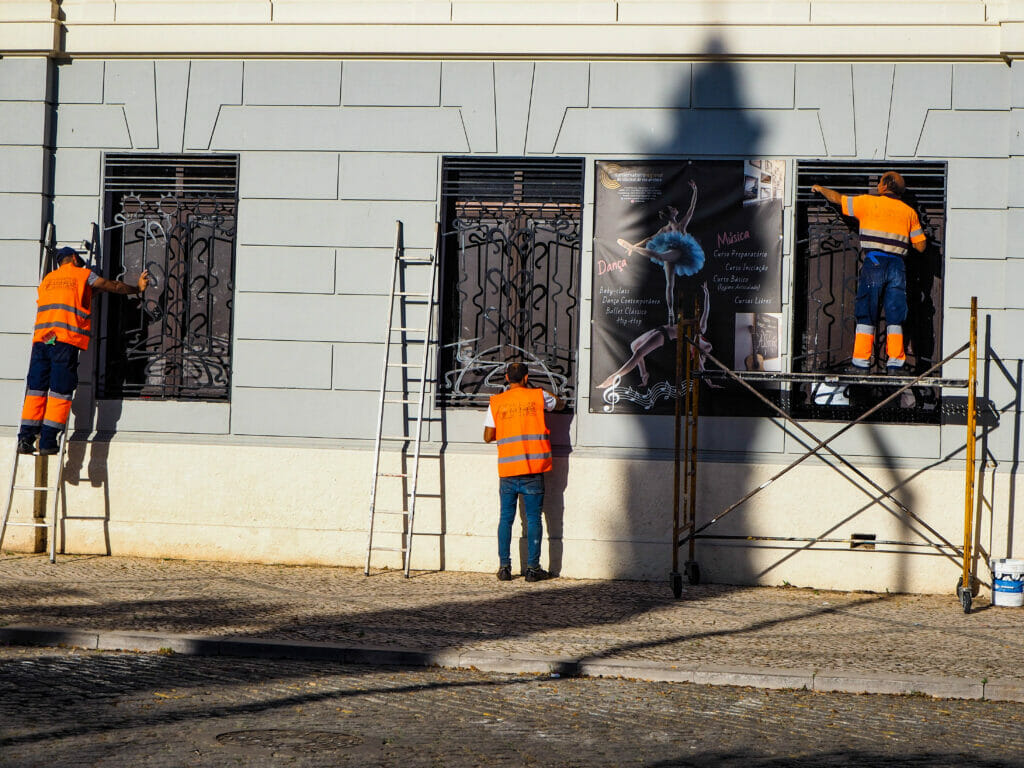 Three men wearing orange safety vests working on a building.