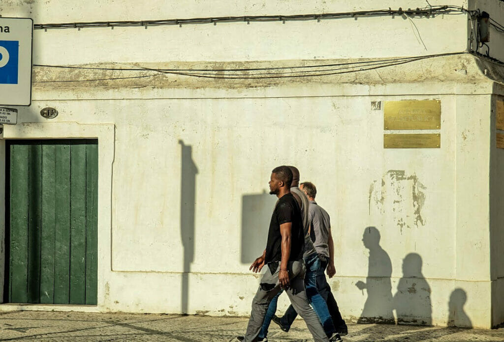 People walking down a street with their shadows cast on a wall.