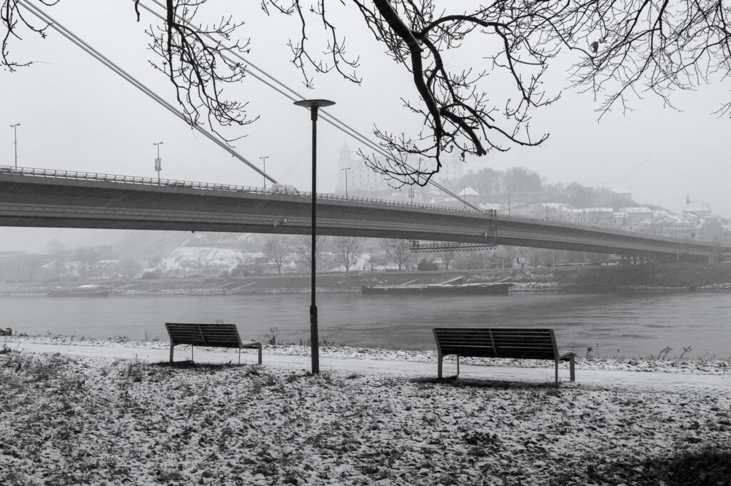 Empty benches in front of a river during a blizzard.