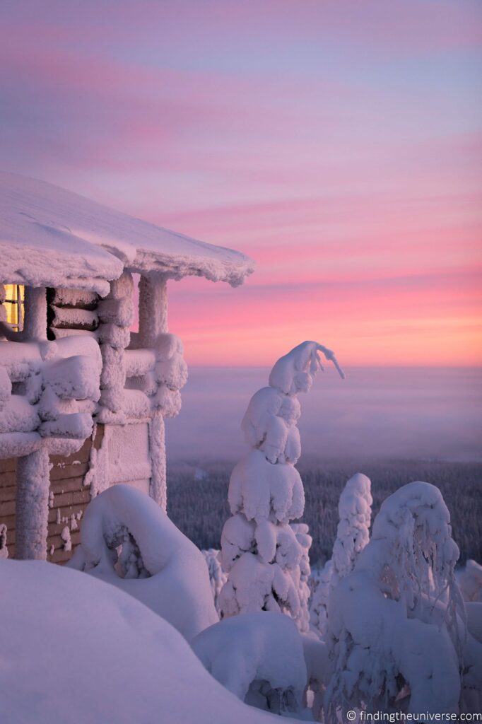 Snow covered trees next to a cabin.