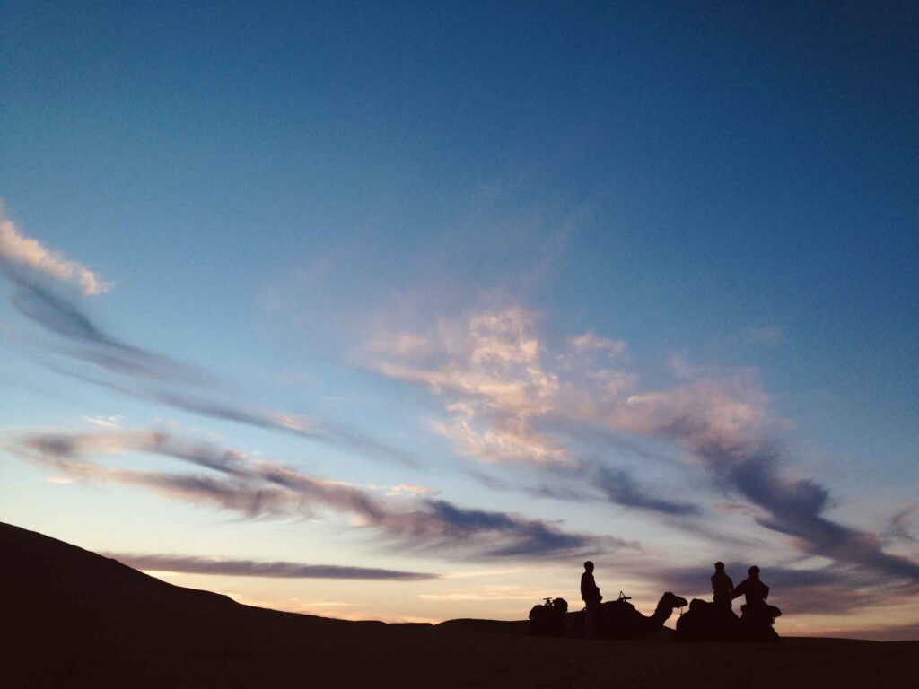 A silhouette of people riding camels in front of a sunset.