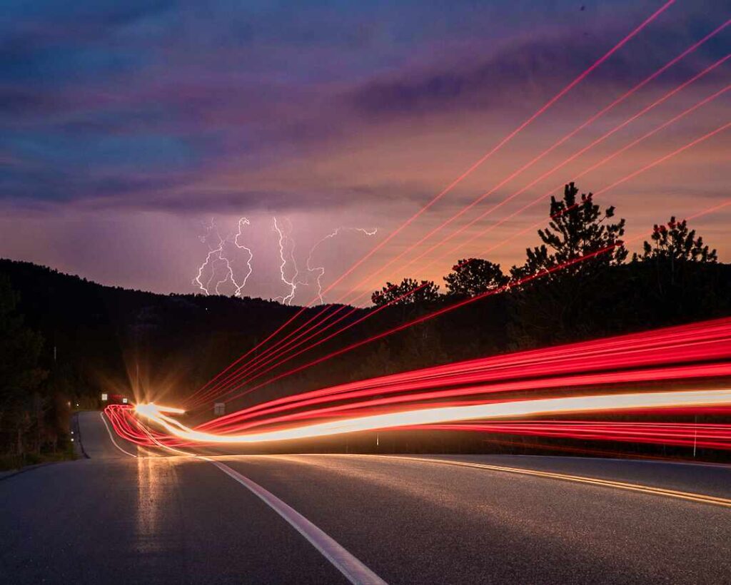 A road with blurred red lights from cars and lightning striking.