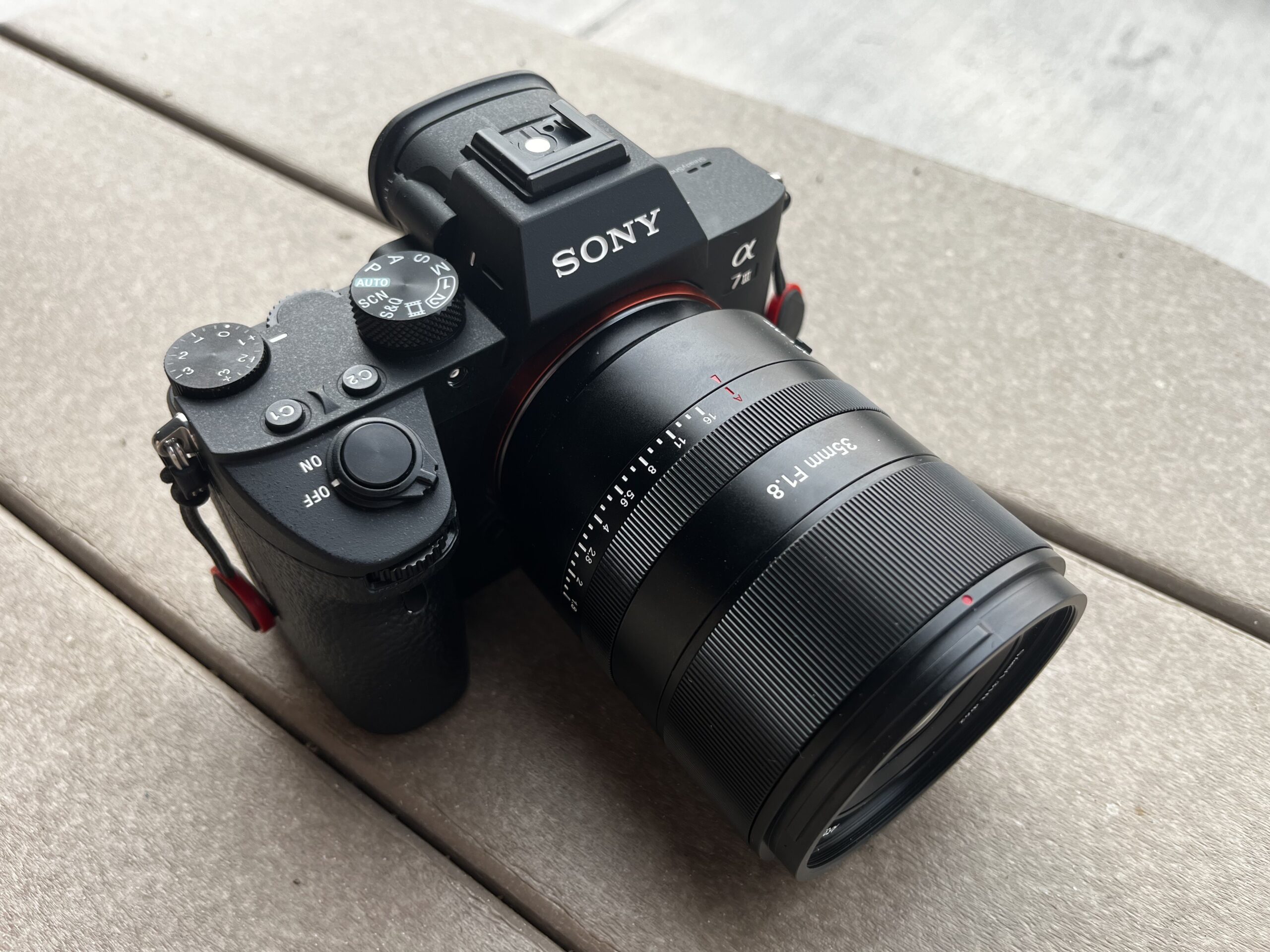 The 7Artisans AF 35mm F1.8 Full Frame Lens on a Sony a7 III camera body on a brown outdoor table.