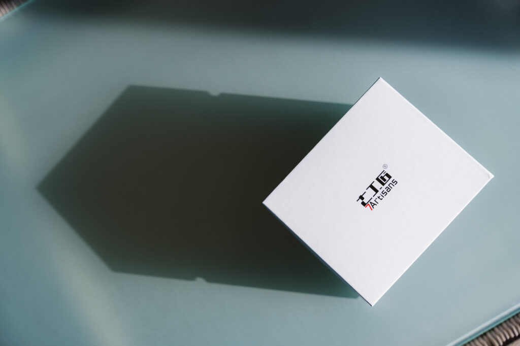 The top of a 7Artisans lens box from above on a glass table with a shadow.