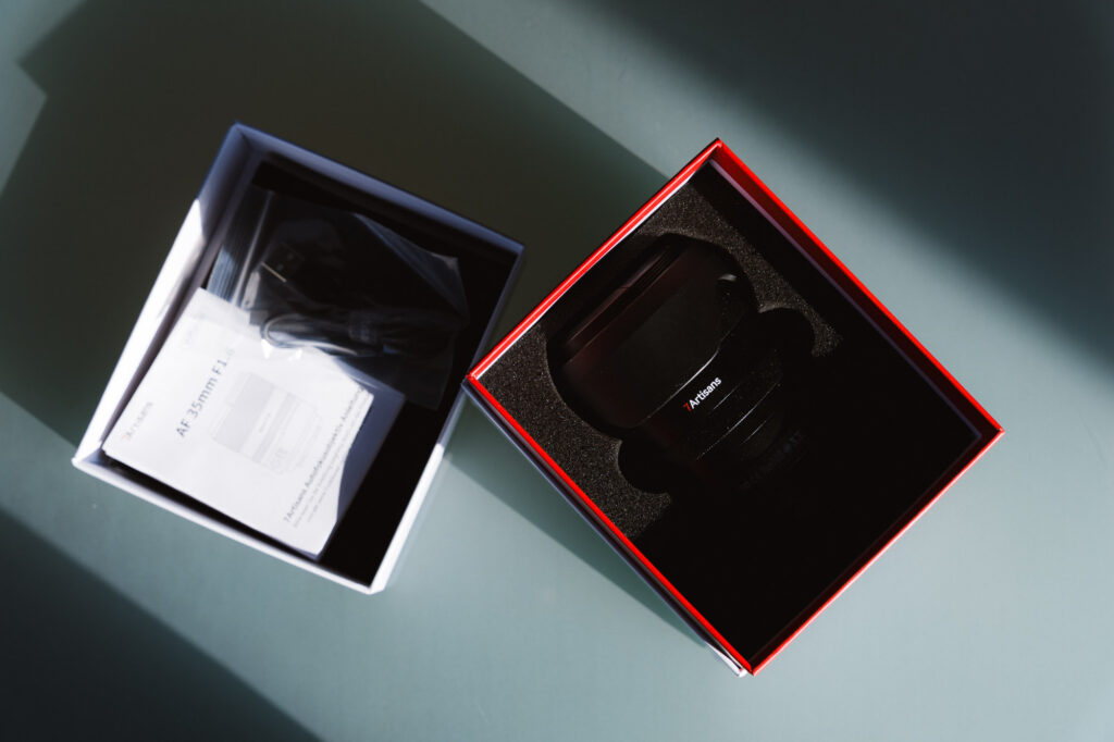 The 7Artisans AF 35mm f/1.8 Full Frame Lens in its original box with the lid open showing the manual.