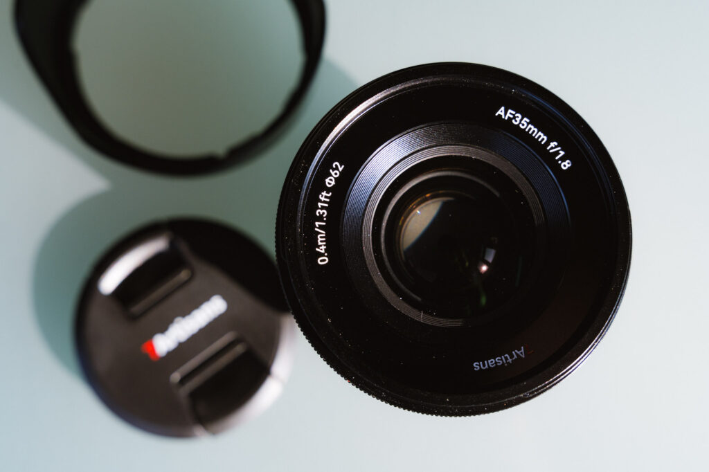 The front element of the 7Artisans AF 35mm f/1.8 Full Frame Lens next to its lens cap and lens hood.